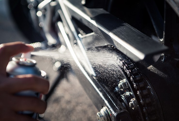 Hand spraying lubricant on motorcycle chain 