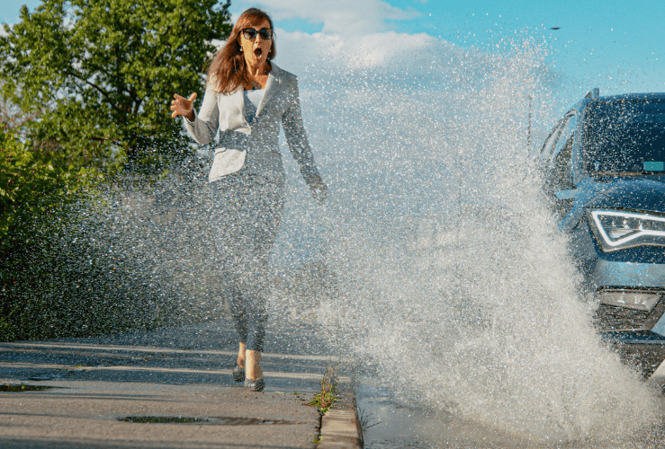 Woman being splashed by car driver driving though puddle