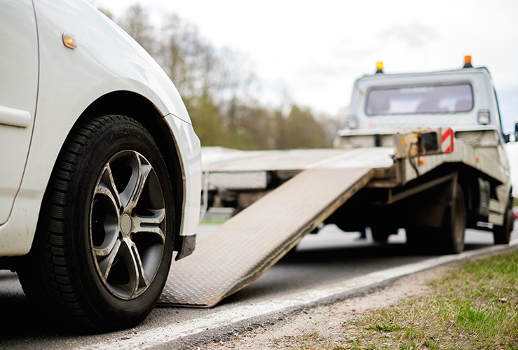 Flat bed truck in front of a broken down car on roadside