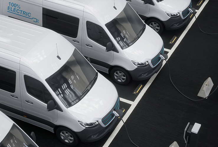 Fleet of generic electric EV delivery vans charging on charging stations